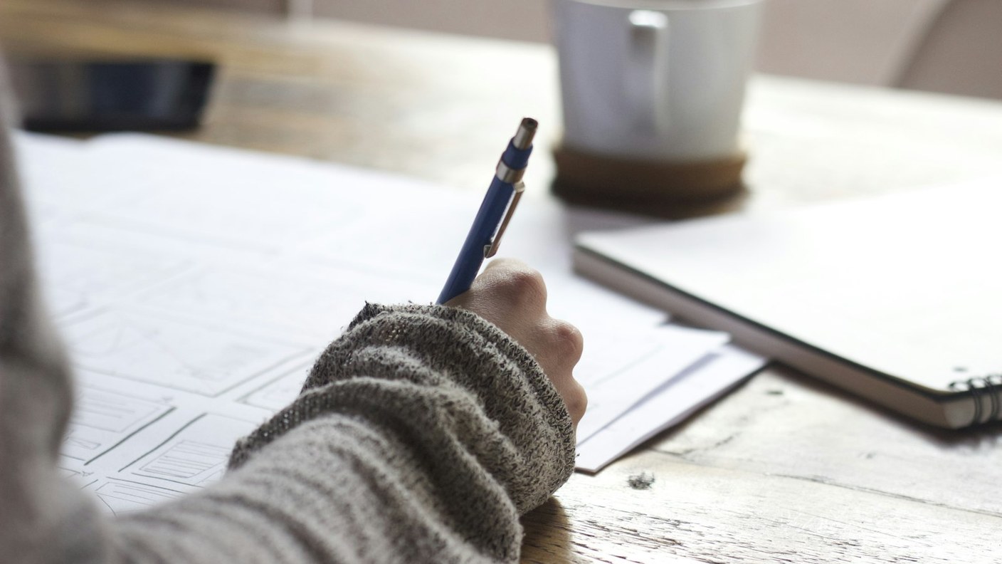 Close documentary photo of a hand writing plans on paper beside a notebook and mug — career planning metaphor.