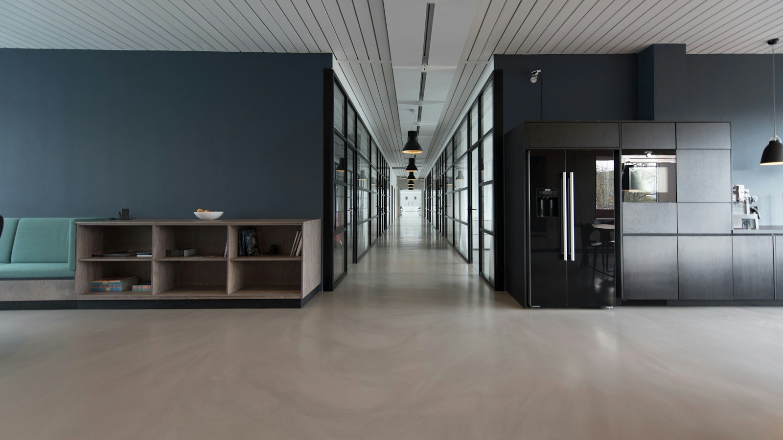 Empty modern office hallway with glass-walled rooms and a kitchenette — a quiet workplace with no one at the desks.