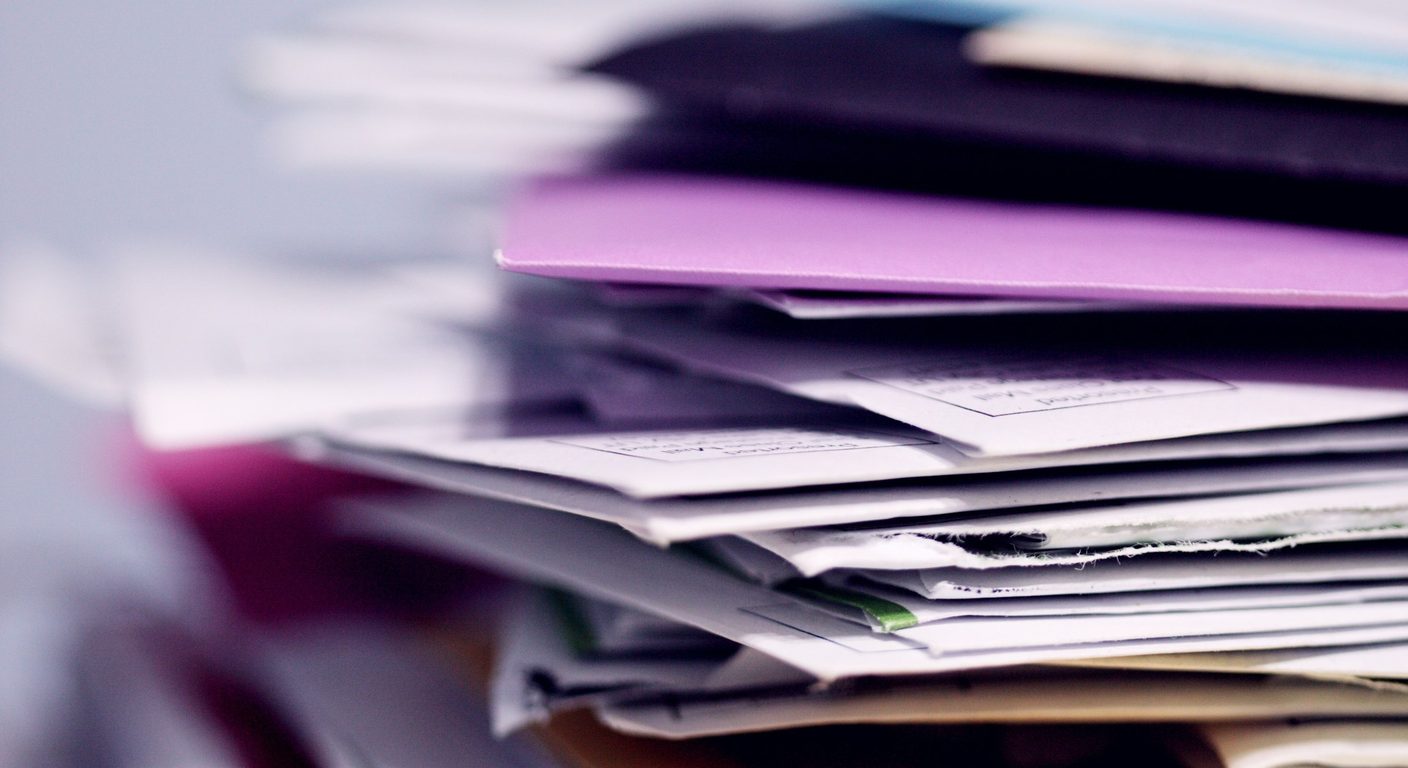 Close-up of a thick stack of white envelopes and folders, including one purple envelope.