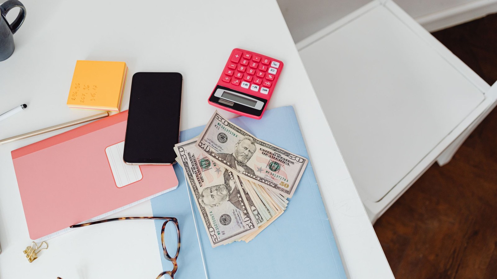 Calculator, cash, folders, phone, and glasses arranged on a desk.
