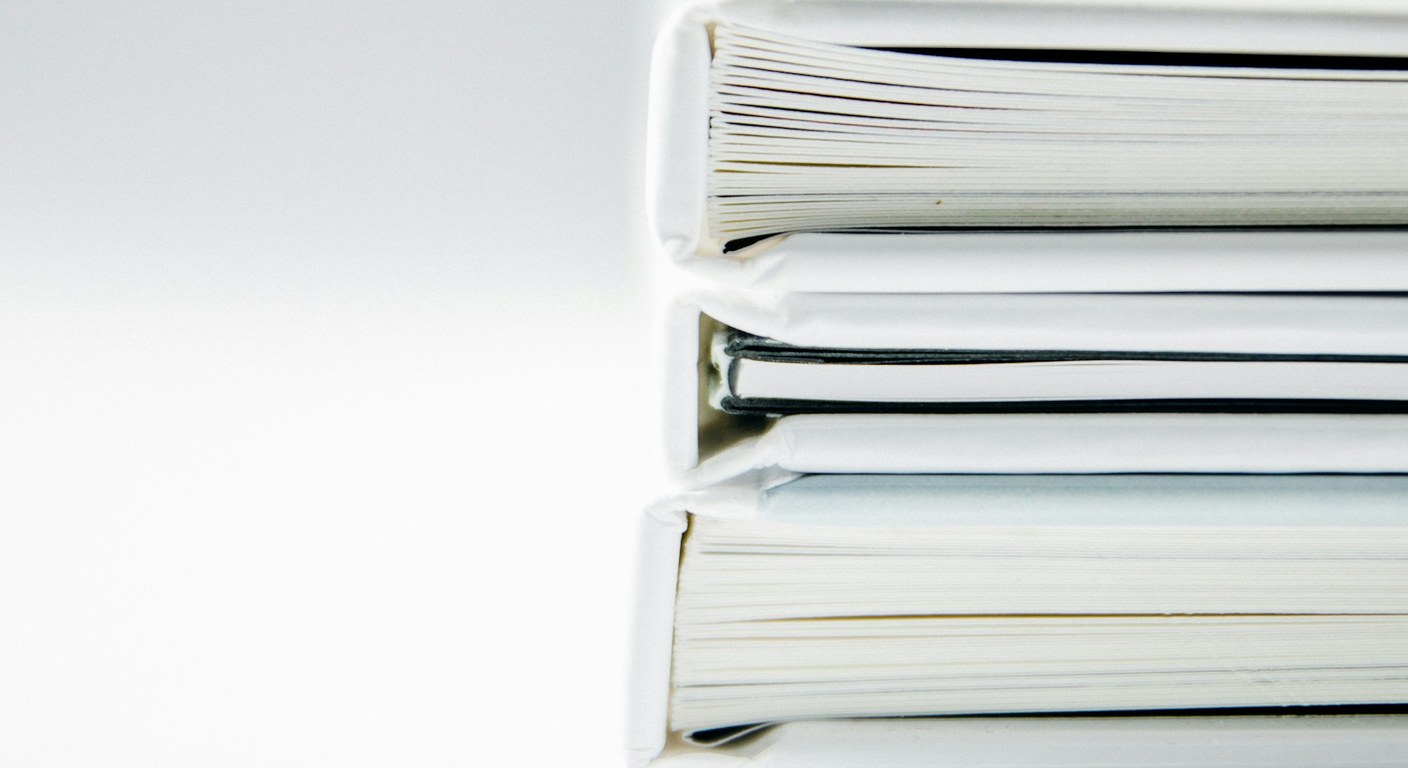 A neat stack of white bound folders on a white desk — an organized packet, not a pile.