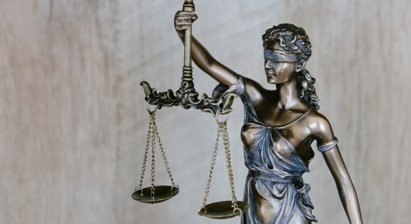 Bronze Lady Justice statue holding balanced scales against a soft neutral background.