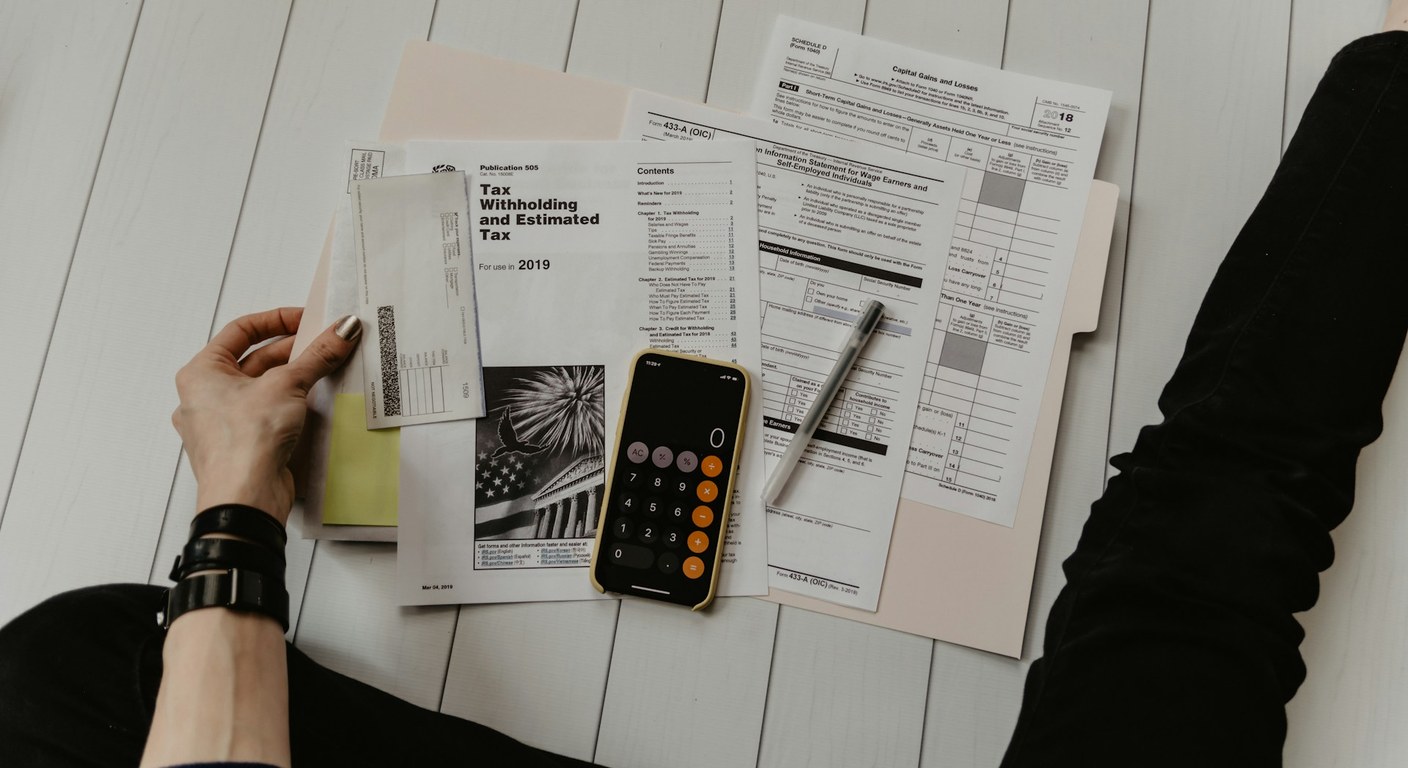 Overhead view of financial and tax paperwork, a phone calculator, and a pen on a wooden floor.